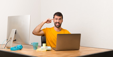 Man working with laptot in a office making the gesture of madness putting finger on the head