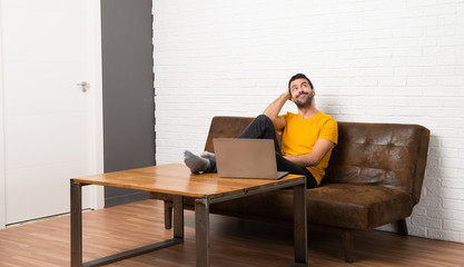 Man with his laptop in a room thinking an idea while scratching head