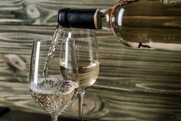 Pouring of wine from bottle into glass on wooden background