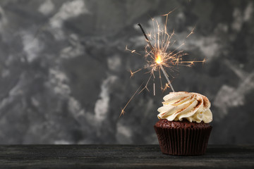 Tasty chocolate cupcake with sparkler on wooden table against grunge background