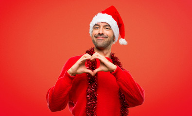 Man with red clothes celebrating the Christmas holidays making heart symbol by hands on red...