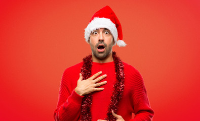Man with red clothes celebrating the Christmas holidays surprised and shocked while looking right...