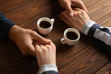 Loving young couple with cups of coffee on wooden background
