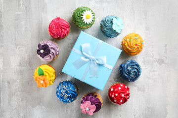 Tasty cupcakes and birthday gift on grey background