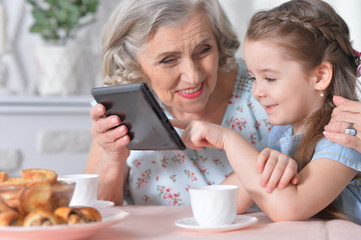 Cute little girl with her grandmother looking at tablet 