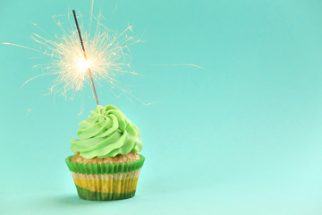 Tasty birthday cupcake with sparkler on color background