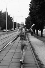 street photo in the style of an old black and white film with grain - a woman is walking along the tram rails in the city