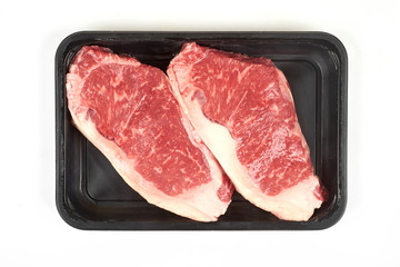 Raw sirloin beef steak in plastic packaging tray.