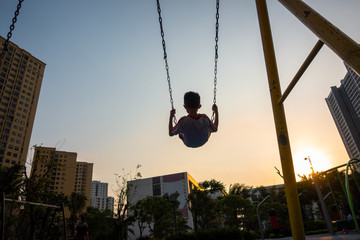 Child swinging on swing in sunset in city with building on background
