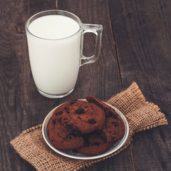 Milk and chocolate cookies on a dark wooden background.