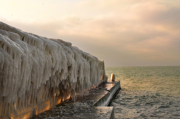 Icy pier in huge icicles on the sea. Winter sea at sunset.
