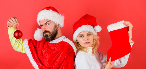 Christmas stocking tradition. Couple christmas santa costume hold sock and ornament ball. Woman and bearded man in santa hat waiting christmas red background. Christmas celebration concept