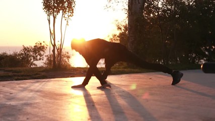 A young sportsman in black sportswear training outdoors. Healthy lifestyle concept, man doing push ups with jumps and cross actions. Sunrise early morning on the background