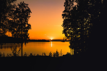 Bright orange sunset across a lake with dark silhouettes of trees