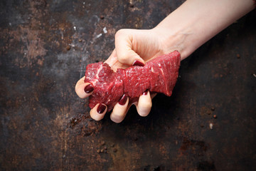 Polędwica wołowa. Kobieta ściska w dłoni kawałek surowego mięsa wołowego. - obrazy, fototapety, plakaty