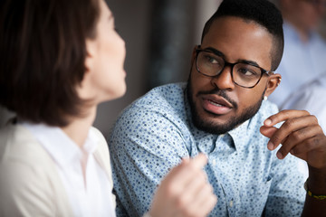 Close up of multiracial colleagues chat talking or discussing something in office, black man speak...