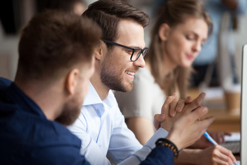 Close up of male colleagues cooperating in coworking office space talking laughing together,...