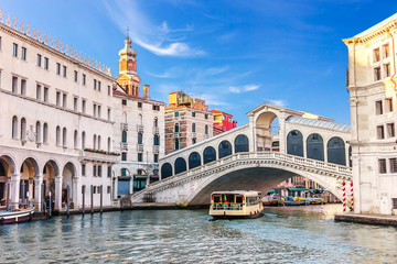 Fototapeta na wymiar Vaporetto under the Rialto Bridge near the Fondaco dei Tedeschi, Palazzo dei Camerlenghi and the dome of San Bartolomeo in Venice