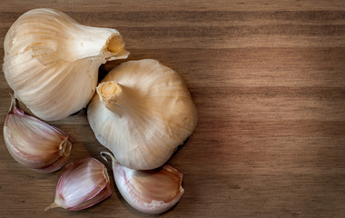 Top view of two whole garlic heads and loose garlic cloves on wooden surface with space for text.