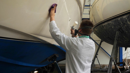 A young man (guy) is a specialist in cleaning the yacht, in a respirator and using a spray on the...