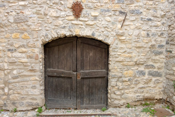 Fototapeta na wymiar Closed the arched wooden door in a wall made of pieces of rock stones. Unused entrance of the ancient fortress in an Italian city