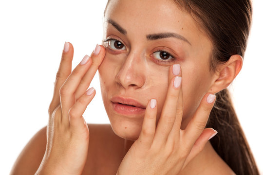 young beautiful girl applying concealer with fingers under her eyes on white background