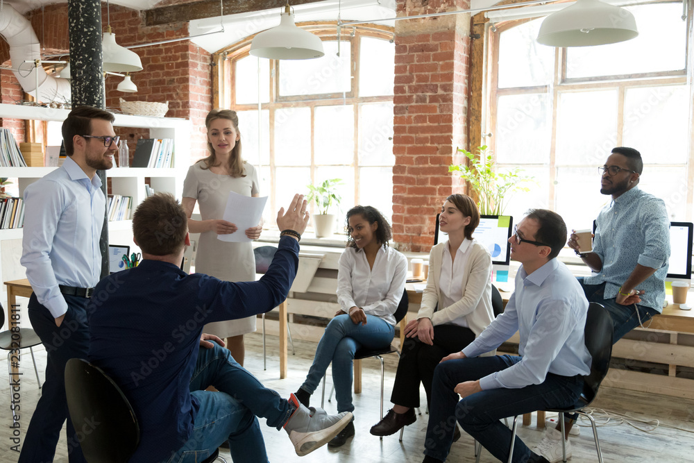 Wall mural ambitious male employee raise hand ask question to female presenter at meeting, man show activity at