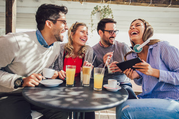 Group of four friends having fun a coffee together. Two women and two men at cafe talking laughing and using digital tablet.