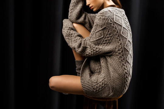 Partial Vie Of Woman In Woolen Grey Sweater Sitting On Bar Stool On Black Background