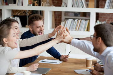 Excited millennial employees give high five celebrating shared win or team success, happy colleagues join hands involved in teambuilding activity at meeting, workers motivated for success show unity