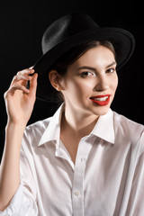 stylish smiling model with red lips in white shirt and black hat posing isolated on black