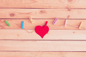 Red heart with clothespins on a rope. Wooden background. Love