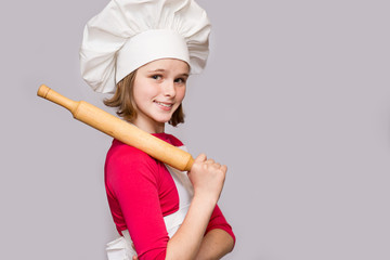 Children cook. Happy little girl in chef uniform holds rolling pin isolated on white background.