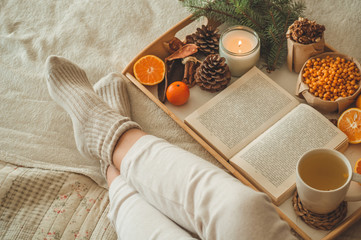 Cozy winter evening , warm woolen socks. Woman is lying feet up on white shaggy blanket and reading book. Cozy leisure scene