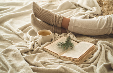 Cozy winter evening , warm woolen socks. Woman is lying feet up on white shaggy blanket and reading book. Cozy leisure scene
