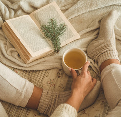 Cozy winter evening , warm woolen socks. Woman is lying feet up on white shaggy blanket and reading book. Cozy leisure scene