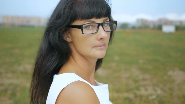 Young woman with in white dress on a windy day on the outskirts of the city of New Yor. Portrait of a businesswoman with glasses looking at the camera. Closeup. Slow Motion.