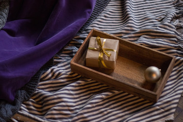 Christmas composition of gift box wrapped in craft paper and decorated with gold ribbon in tray. Selected focus