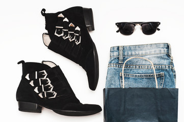 Blue jeans in a paper bag, black suede boots with buckles and sunglasses on a white background....