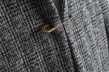 Grey winter coat pinned on safety pin. Bad clothes repair. Closeup.