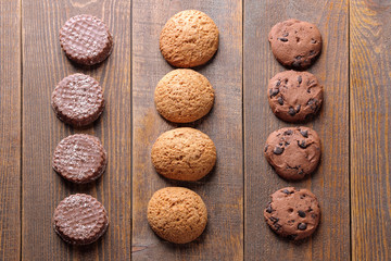 Different tasty cookies piled in a row on a brown wooden table. view from above