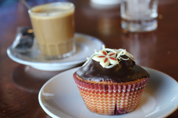 A close view of a chocolate muffin on a plate with a coffe cup on background (cafè con leche) on a table in Zaragoza, Spain