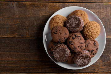 different tasty cookies on a plate on a brown wooden table. top view with space for inscription