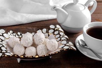 Tasty sweet coconut candies in a vase with tea on a brown wooden table.