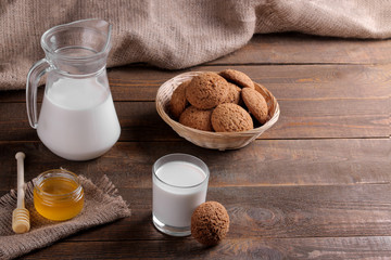 Tasty sweet oatmeal cookies with milk and honey on a brown wooden table.