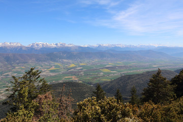 A landscape of snow-clad Pyrenees mountains and a wide valley with blue cloudy sky and some bushes in Pe&ntilde;a Oroel, Aragon region, Spain