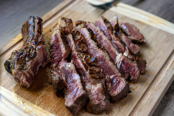 Grilled ribeye beef steak is cutted witn knife. Baked juicy fillet in slices on a wooden table. Medium well
