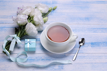 Beautiful white flowers. Eustoma bouquet with tea and gift on a blue wooden table.