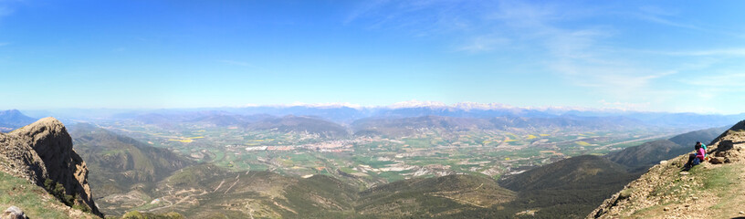Fototapeta na wymiar A wide angle landscape of snow-clad Pyrenees mountains and a wide valley with blue cloudy sky and some bushes in Peña Oroel, Aragon region, Spain