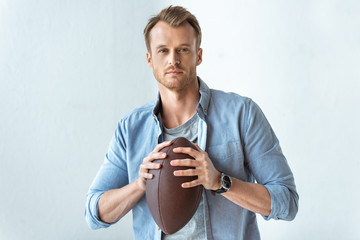 confident handsome man holding rugby ball and looking at camera near wall - Powered by Adobe